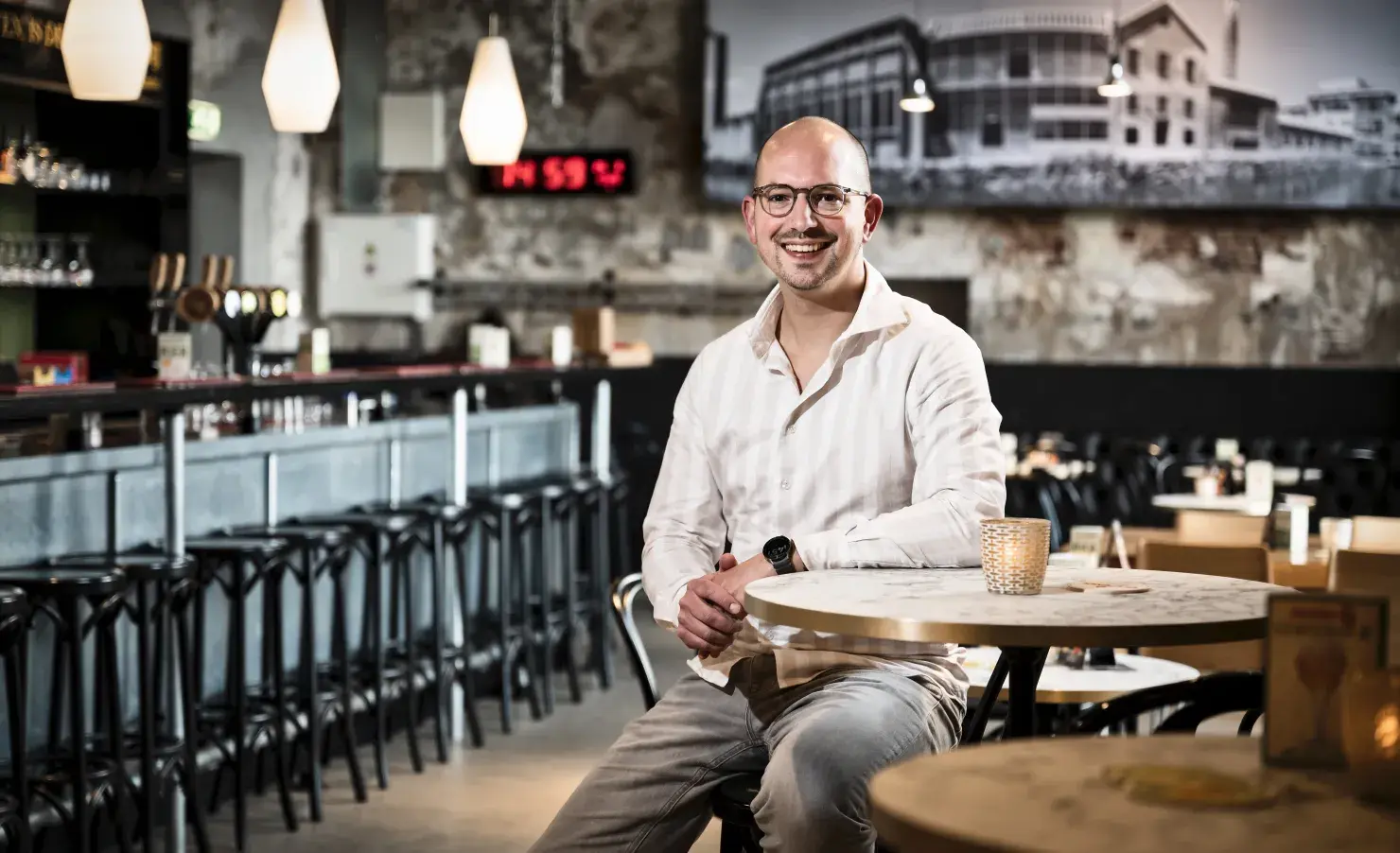 Man in cafe, zittend aan tafel en lachend naar de camera