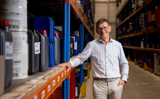 Man poserend voor de camera in transportmagazijn tussen stellingkasten