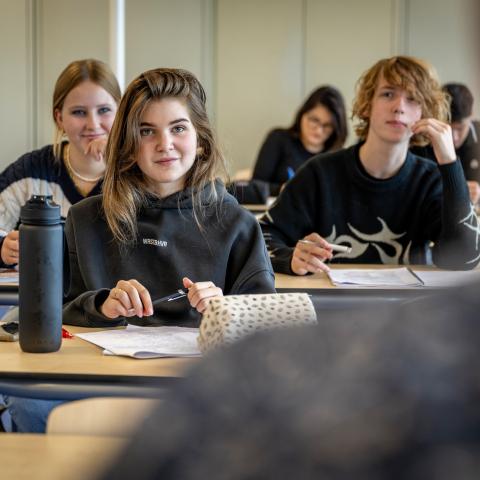 Meisje aan bureau in klaslokaal omringd door klasgenoten