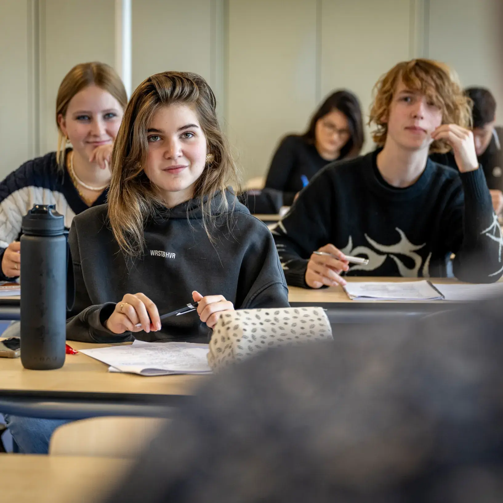 Meisje aan bureau in klaslokaal omringd door klasgenoten