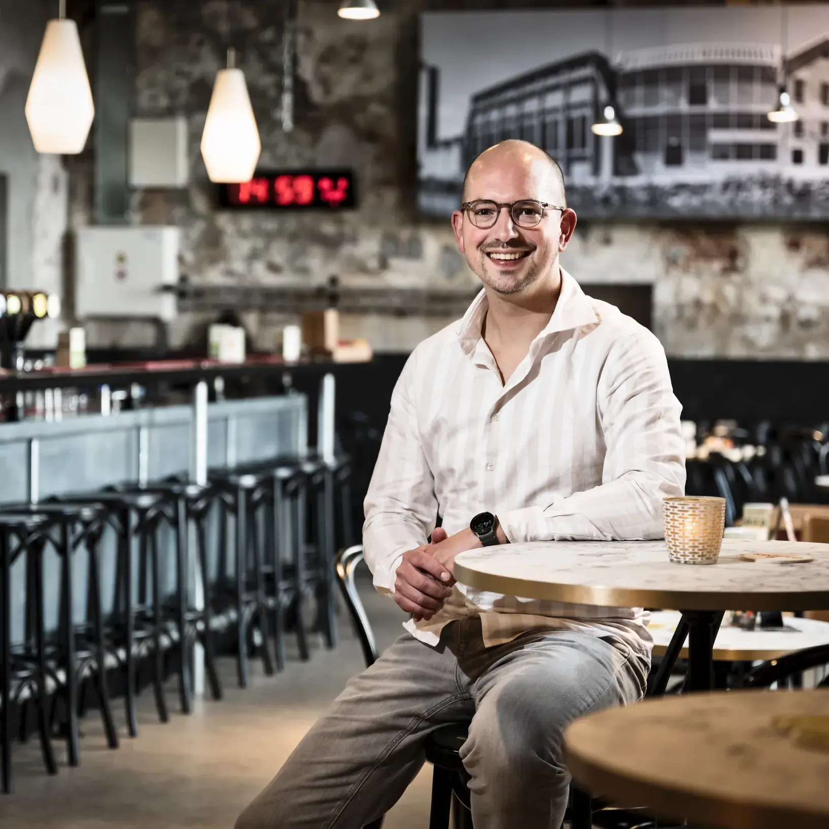 Man in cafe, zittend aan tafel en lachend naar de camera